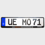 Foto eines Kennzeichenhalters mit einer schwarzen Leiste mit einem zweifarbigen Aufdruck von "www.bedruckte-kennzeichenhalter.de" und dem Media Orange Logo