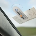 Weißer Parkscheinhalter mit Media Orange Logo an der Autoscheibe befestigt und als Halter für Parkscheine genutzt